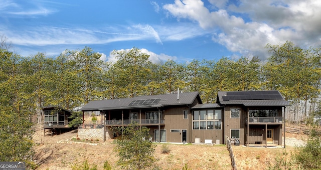 back of property featuring roof mounted solar panels, metal roof, and a balcony