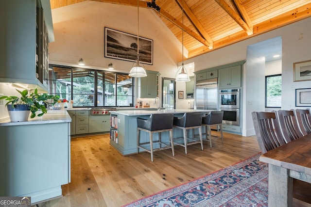 kitchen with stainless steel appliances, beam ceiling, green cabinets, and light wood-style flooring