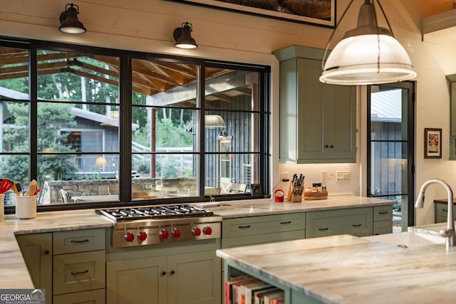 kitchen with stainless steel gas cooktop, decorative light fixtures, light stone countertops, and a sink