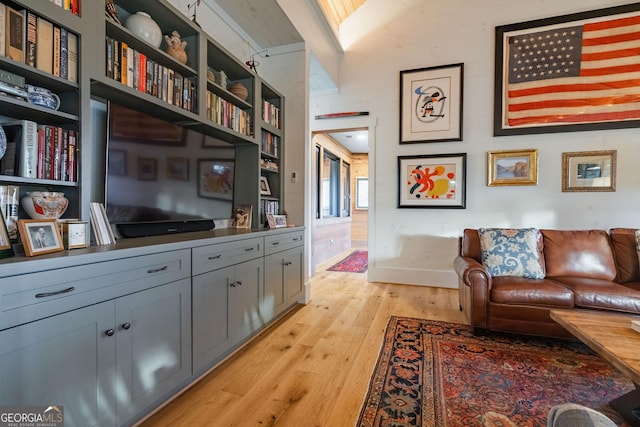 living area with baseboards, lofted ceiling, and light wood-style floors