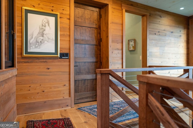 hallway featuring an upstairs landing, wood finished floors, and wood walls