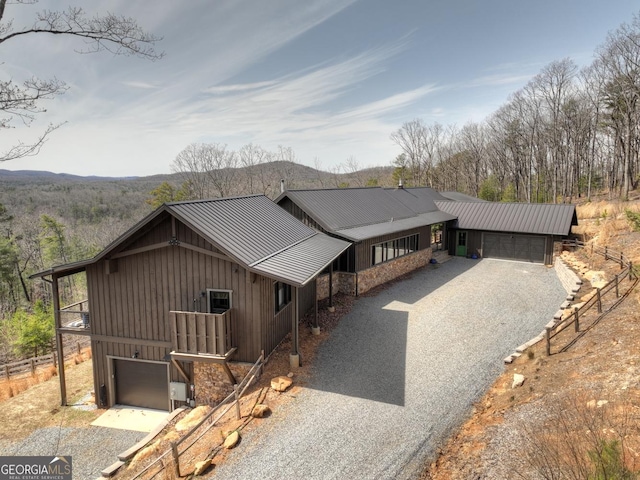 rustic home featuring board and batten siding, fence, metal roof, a garage, and driveway