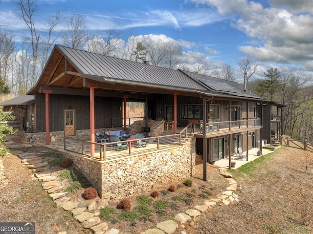 back of property featuring a standing seam roof, roof mounted solar panels, metal roof, and a patio