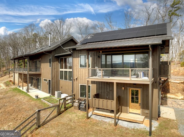 back of house featuring a patio area, roof mounted solar panels, metal roof, and a balcony