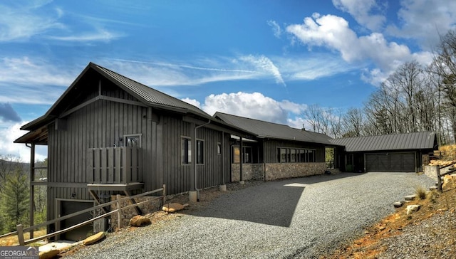 view of home's exterior with driveway, stone siding, board and batten siding, an attached garage, and metal roof