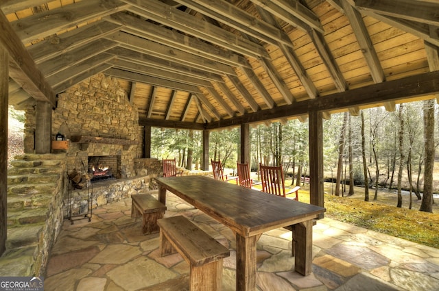 sunroom / solarium with lofted ceiling with beams, an outdoor stone fireplace, and wood ceiling