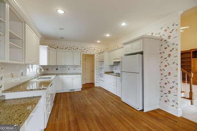 kitchen featuring white appliances, wood finished floors, light stone countertops, a sink, and crown molding