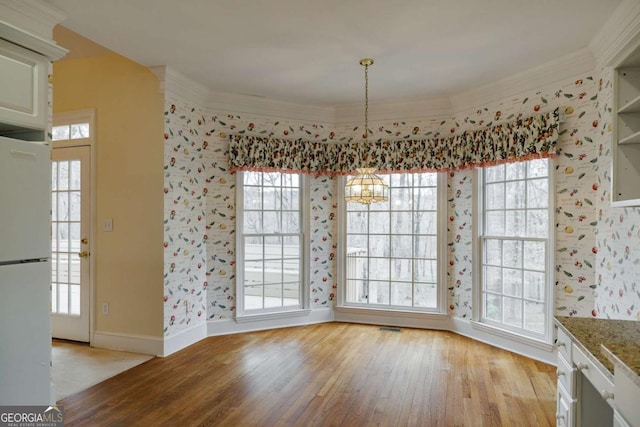 unfurnished dining area featuring an inviting chandelier, crown molding, visible vents, and light wood finished floors