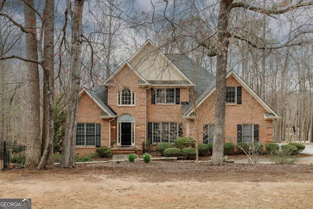 view of front facade with fence, brick siding, and a shingled roof