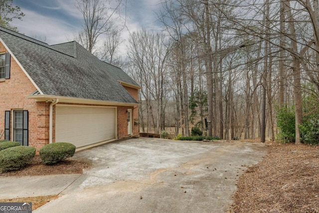 view of home's exterior featuring concrete driveway, an attached garage, brick siding, and roof with shingles