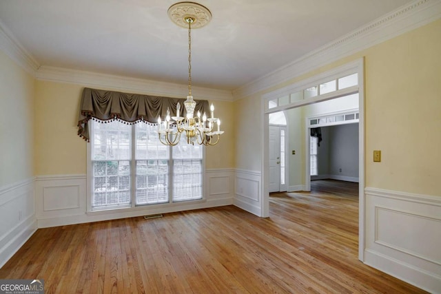 unfurnished dining area with light wood finished floors, a chandelier, visible vents, and ornamental molding