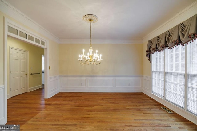 unfurnished dining area with crown molding, light wood-type flooring, visible vents, and a chandelier