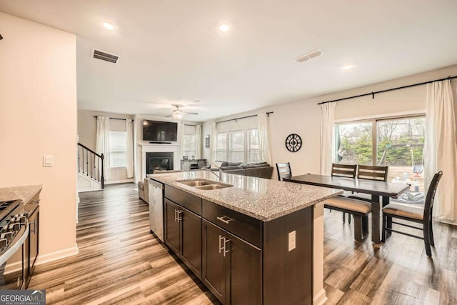 kitchen featuring light wood-type flooring, visible vents, a sink, a glass covered fireplace, and dark brown cabinets