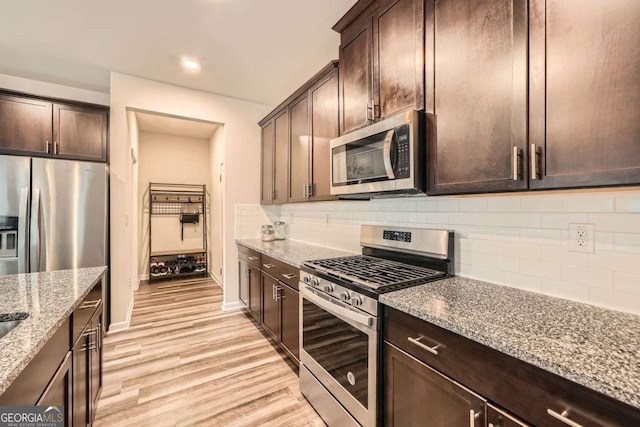 kitchen with stainless steel appliances, light stone countertops, dark brown cabinetry, and light wood finished floors