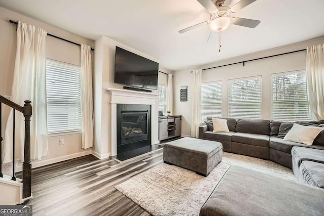 living room featuring wood finished floors, stairway, a fireplace, baseboards, and ceiling fan