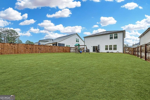 back of property with a playground, a yard, and a fenced backyard