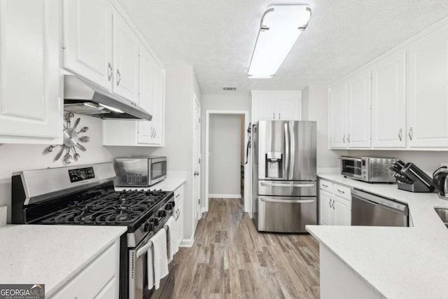 kitchen featuring under cabinet range hood, light wood-style flooring, appliances with stainless steel finishes, white cabinets, and a textured ceiling