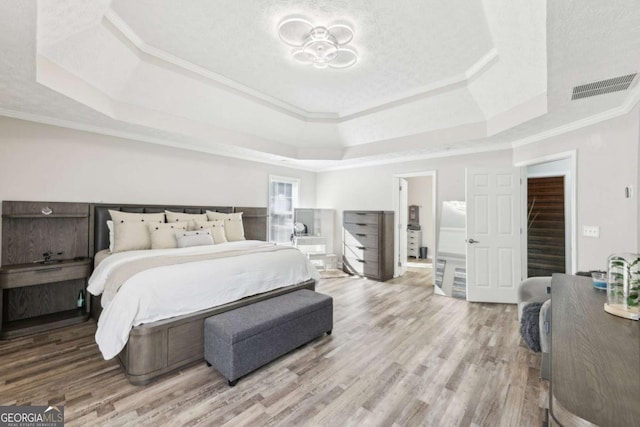 bedroom featuring a tray ceiling, wood finished floors, visible vents, and ornamental molding