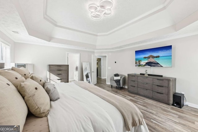 bedroom featuring a tray ceiling, a notable chandelier, wood finished floors, and baseboards