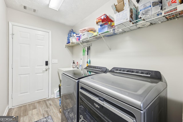 laundry area featuring visible vents, a textured ceiling, washing machine and dryer, light wood finished floors, and laundry area