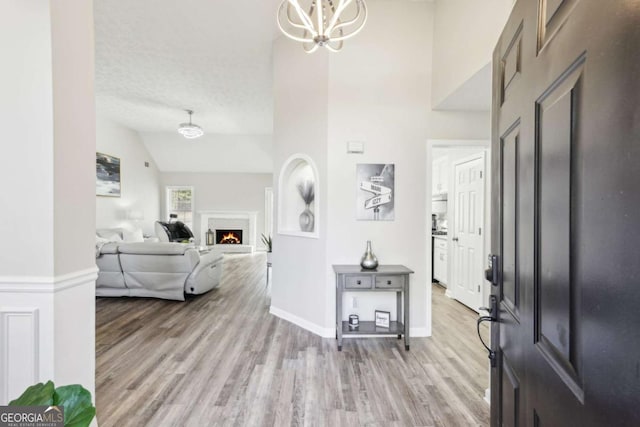 entryway with high vaulted ceiling, light wood-style flooring, a warm lit fireplace, an inviting chandelier, and a textured ceiling