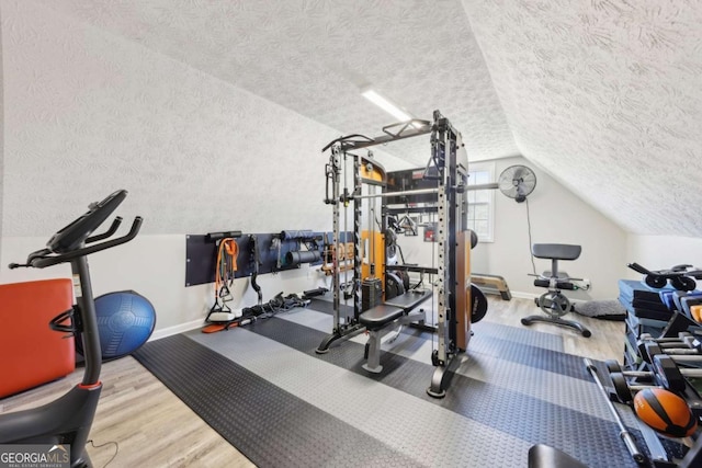 workout room featuring lofted ceiling, wood finished floors, baseboards, and a textured ceiling