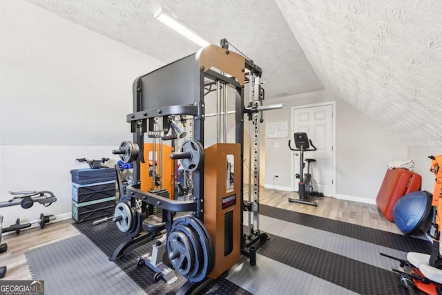 workout room with vaulted ceiling, wood finished floors, baseboards, and a textured ceiling