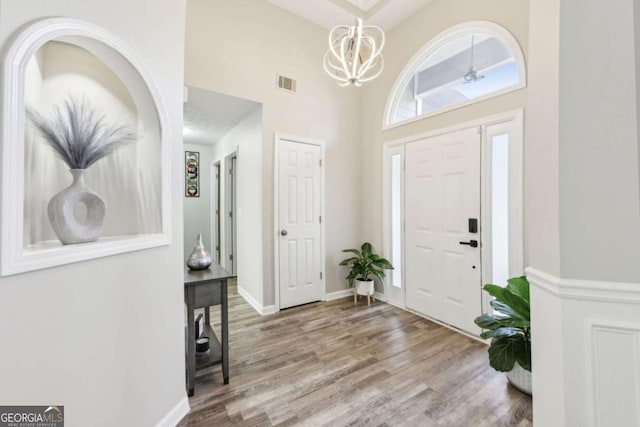 entrance foyer with visible vents, baseboards, a high ceiling, an inviting chandelier, and wood finished floors