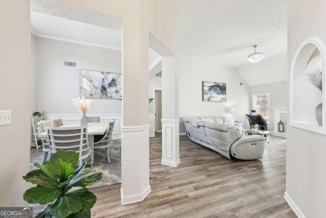 living area featuring visible vents, a textured ceiling, wood finished floors, and vaulted ceiling