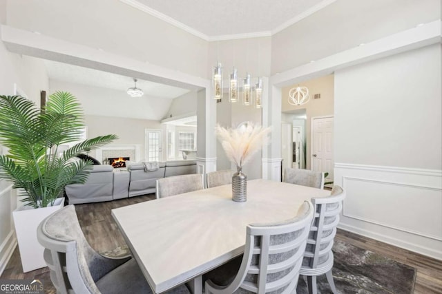 dining room featuring crown molding, dark wood-type flooring, a lit fireplace, wainscoting, and a decorative wall