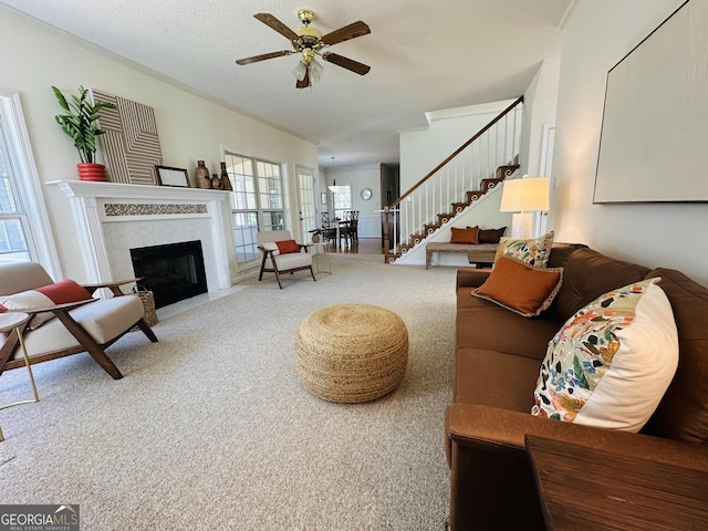 carpeted living room with stairway, a fireplace, ceiling fan, a textured ceiling, and crown molding