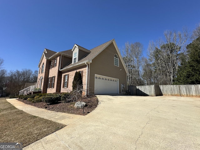 view of side of property featuring a garage, fence, brick siding, and driveway