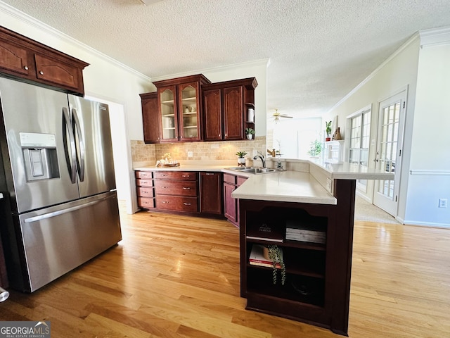 kitchen featuring open shelves, a peninsula, a sink, light wood-style floors, and stainless steel fridge