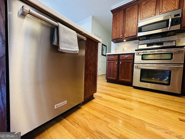 kitchen featuring double wall oven, light countertops, stainless steel microwave, light wood-type flooring, and backsplash