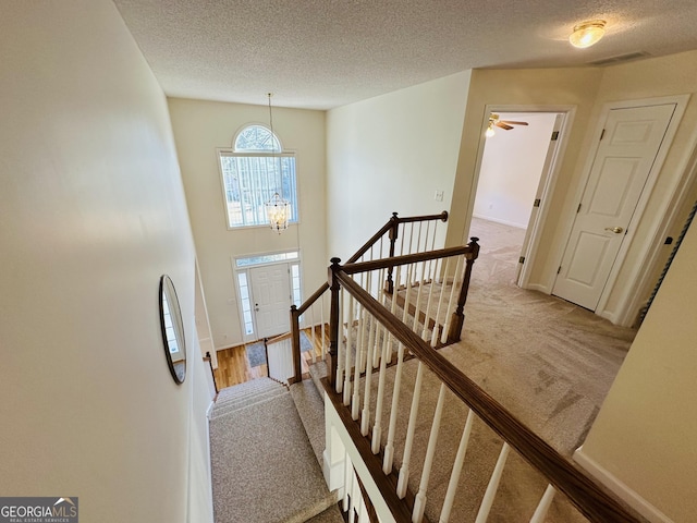 staircase with visible vents, a textured ceiling, baseboards, and carpet floors