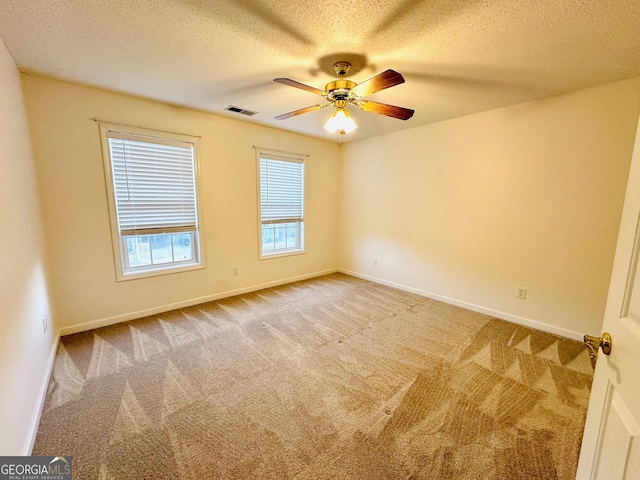 carpeted empty room featuring visible vents, a textured ceiling, baseboards, and a ceiling fan