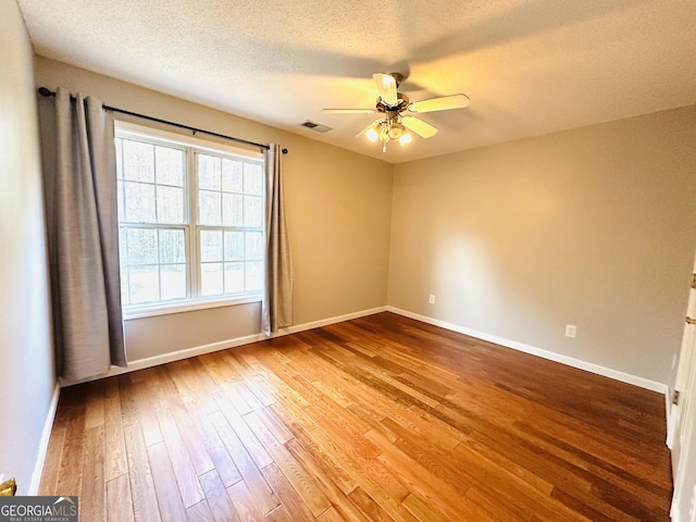 empty room featuring baseboards, wood finished floors, visible vents, and ceiling fan