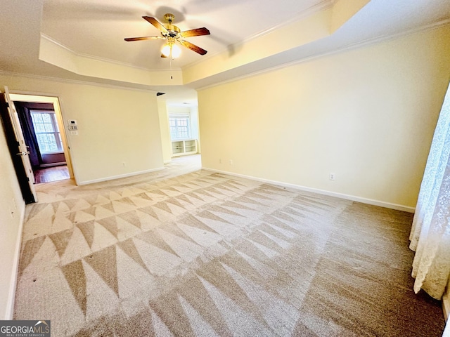 unfurnished room featuring baseboards, a tray ceiling, ceiling fan, light carpet, and crown molding