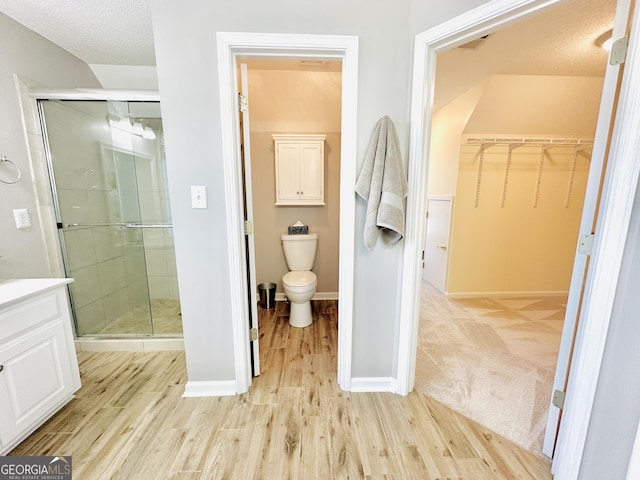 bathroom with a stall shower, toilet, a walk in closet, and wood finished floors