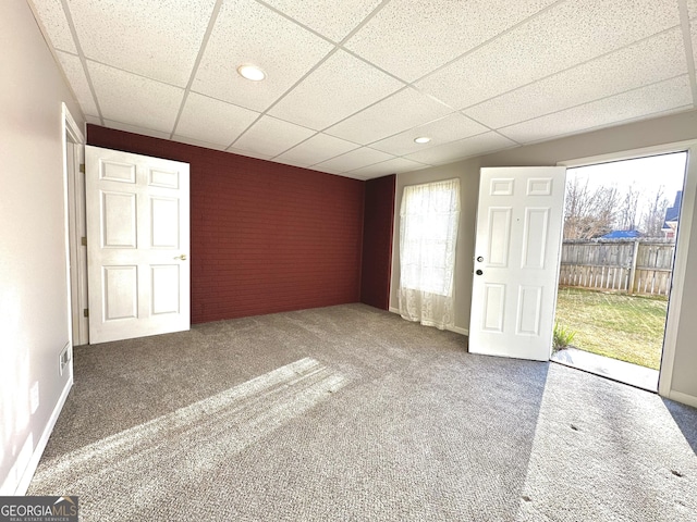 empty room with baseboards, a paneled ceiling, brick wall, and carpet flooring