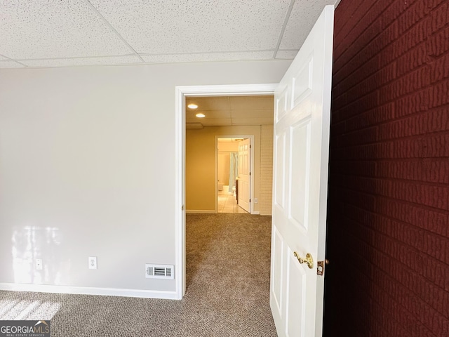 hall with visible vents, a drop ceiling, baseboards, and carpet floors