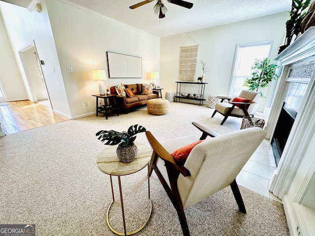 living area with a fireplace with flush hearth, light carpet, ornamental molding, a ceiling fan, and a textured ceiling