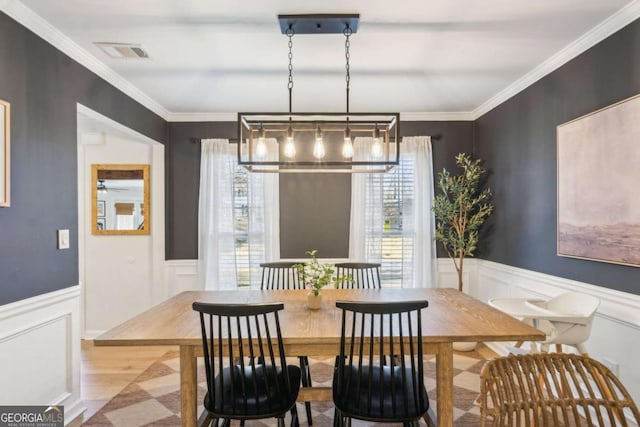 dining space featuring visible vents, crown molding, a wainscoted wall, wood finished floors, and a decorative wall