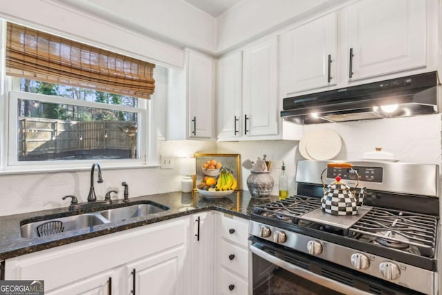 kitchen featuring under cabinet range hood, a sink, dark stone countertops, white cabinetry, and gas stove