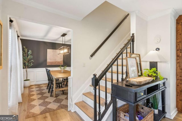 stairs with a decorative wall, crown molding, a wainscoted wall, and wood finished floors