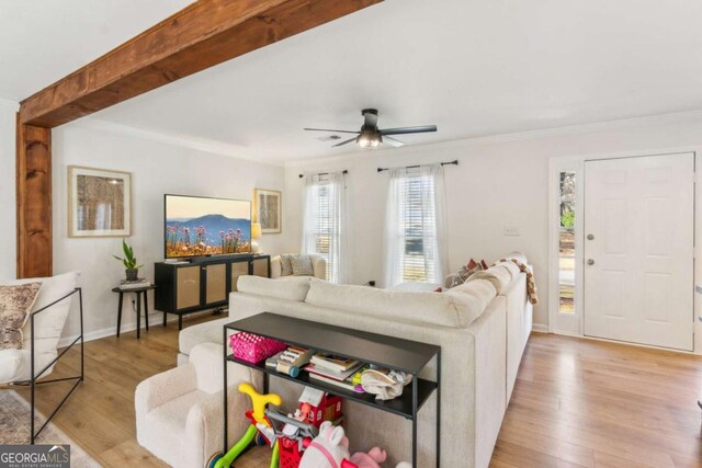 living area with beamed ceiling, light wood-style flooring, crown molding, and baseboards