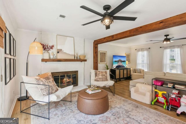 living room featuring visible vents, beam ceiling, wood finished floors, a fireplace, and baseboards