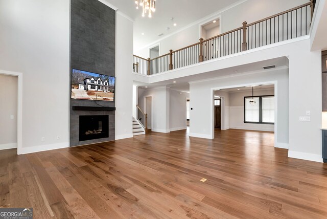 unfurnished living room featuring wood finished floors, visible vents, baseboards, an inviting chandelier, and a tiled fireplace