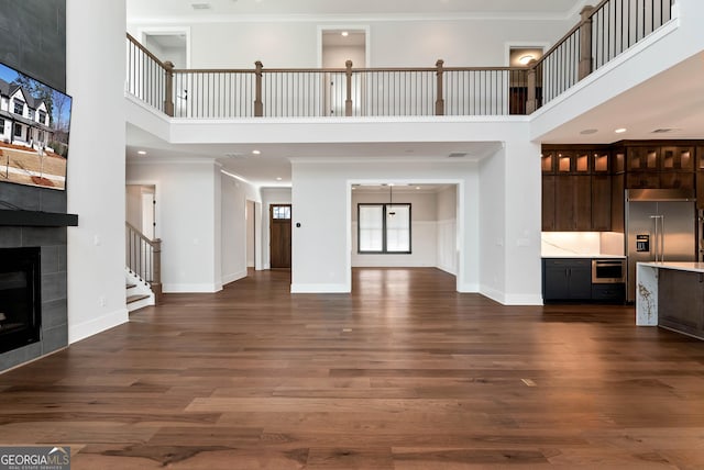 unfurnished living room with a tiled fireplace, dark wood-style floors, crown molding, and baseboards