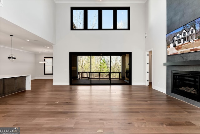 unfurnished living room featuring a tile fireplace, a high ceiling, baseboards, and wood finished floors